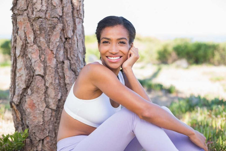 Smiling woman in athletic wear sits outdoors against a tree, radiating health and promoting cholesterol supplements for heart wellness.