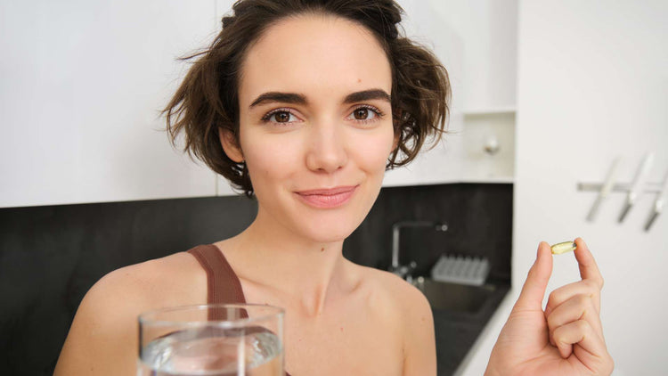 Smiling woman holding a supplement capsule with a glass of water, representing The Good Stuff's Enzyme Process products for wellness support.