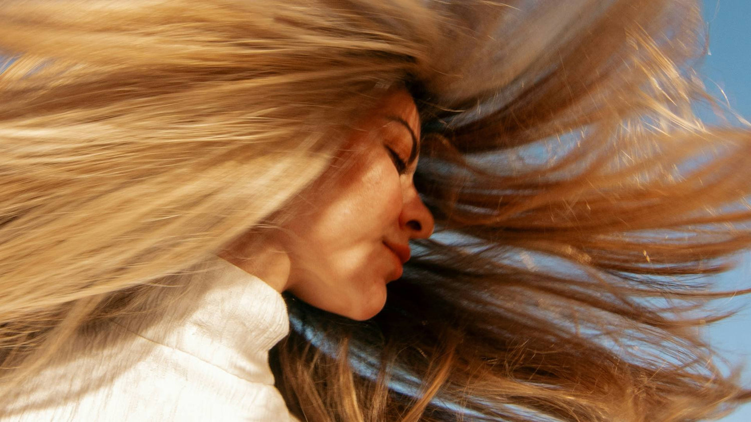 Woman with flowing hair under a clear blue sky, symbolising vitality and potential benefits of hair growth supplements.