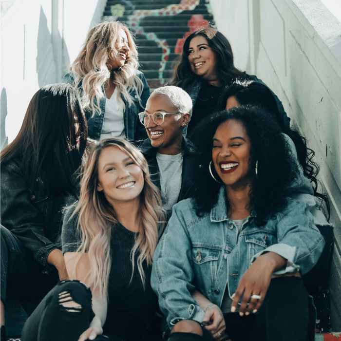 A group of diverse women sitting together on stairs, laughing and enjoying each other's company, reflecting the calming and supportive benefits of Rescue Remedy from The Good Stuff.